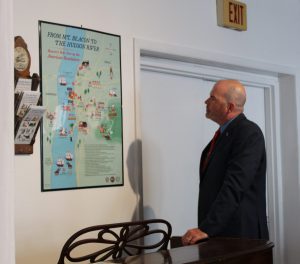 A man in a suit stands near a map titled 'From Mt. Beacon to the Hudson River: Beacon's Role During the American Revolution'.