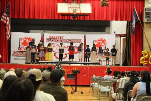 Students pose on stage holding certificates in front of a Liberty Elementary banner