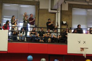 Family members cheer from the raised bleacher in a gym