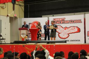 A student holds a certificate as two adults stand near on stage