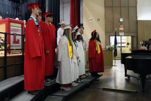 Graduates in red and white gowns stand on risers at Liberty High School.