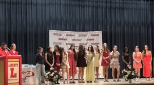 Students stand on a stage in front of a banner that reads 'Liberty Redhawks'.