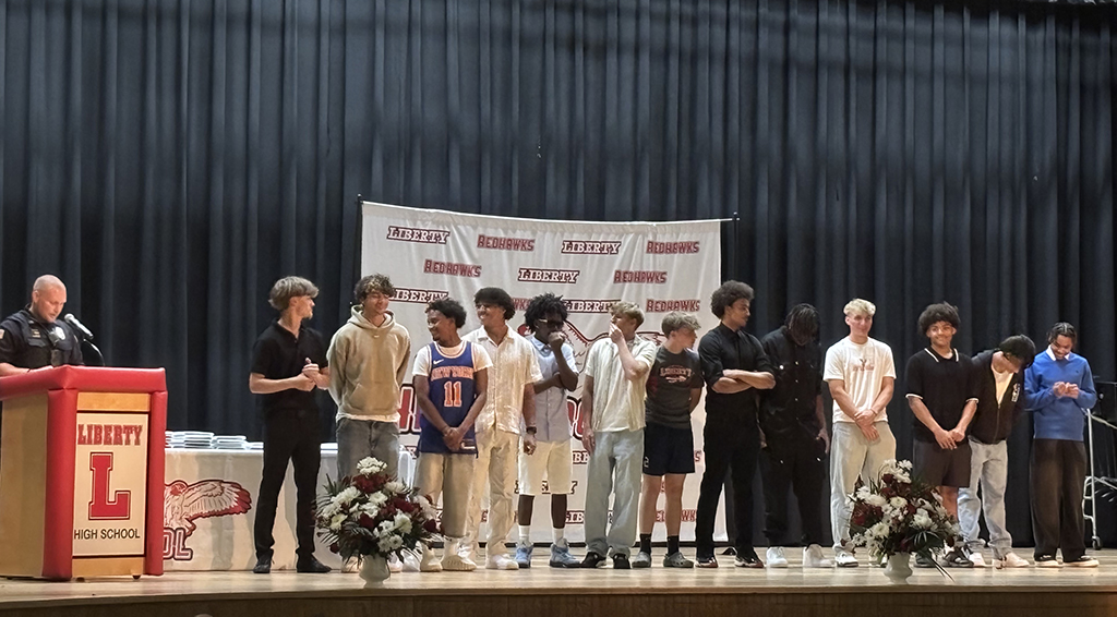 A group of young men stand on a stage in front of a banner that reads 'Liberty Redhawks'.