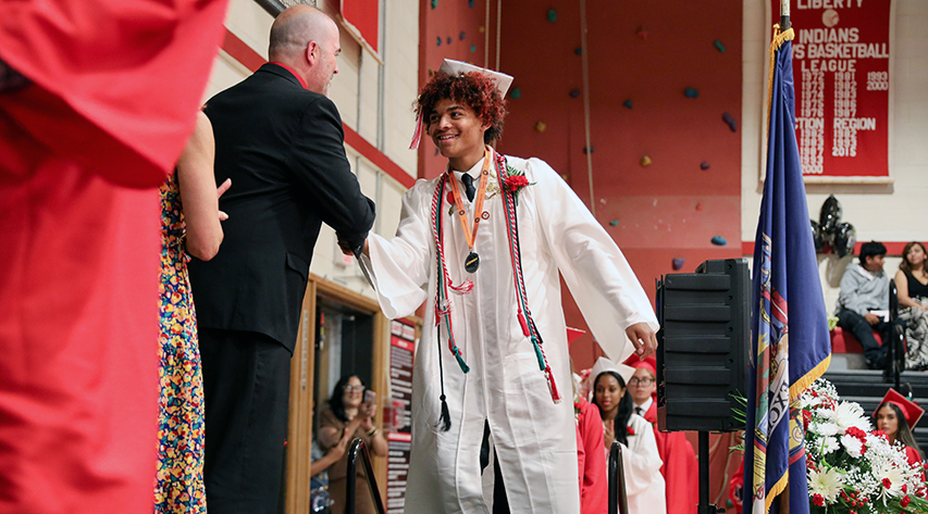 A student in a cap and gown shakes hands with a man in a suit as he crosses the stage.