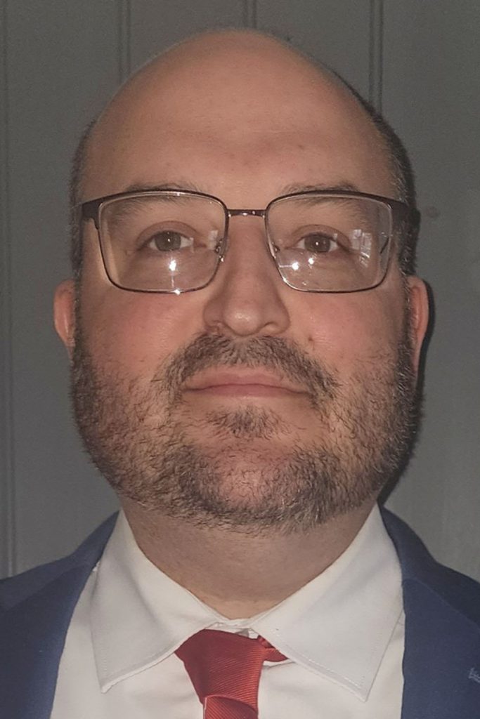 Headshot portrait of Stephen Matuszak, a man with glasses, a shaved head, and a beard.