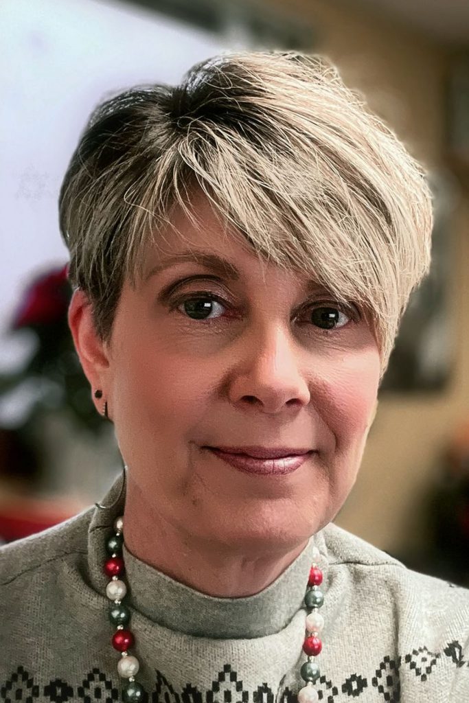 Headshot of stacy feasel, a smiling woman with short, layered blonde hair wearing a grey sweater and a beaded necklace.