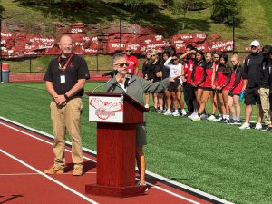 Coach speaking into mic on a podium while pointing to the right