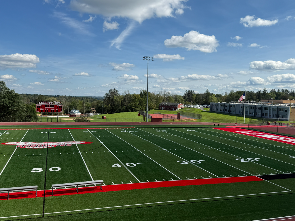 view of football field with the tennis courts and school in background