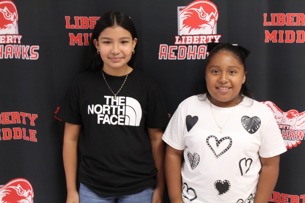 middle school students smiling and standing against a liberty middle school background with the liberty red hawks logo