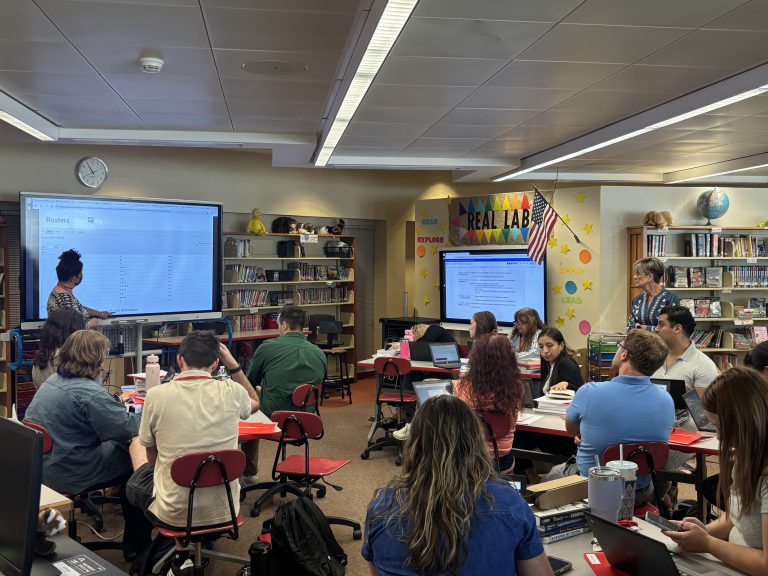 Features another presenter speaking in front of a display screen with attendees seated at tables in the same library setting.