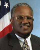 joseph lewis, wearing suit and tie, glasses, smiling and facing camera, with american flag behing him, alumni of liberty and honoree of wall of fame