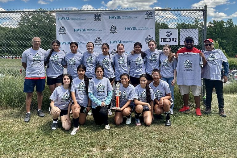 Members of the Liberty United Lady Devils U16 soccer team and their coaches posing together in uniform on a soccer field after winning the Hudson Valley Youth Soccer League championship.